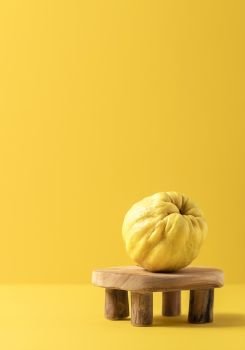 Just one quince fruit, freshly harvested, on a teeny tiny wooden table, isolated on yellow paper background. Tasty golden autumn fruit. Fall fruits.