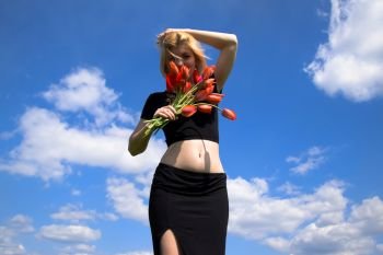 lady with a bouquet of tulips on a background of blue sky with clouds. Young woman with a bouquet of tulips in the field.. lady with a bouquet of tulips on a background of blue sky with clouds.