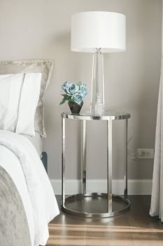 White shade reading lamp and blue rose on glass top stainless steel frame bedside table next to bed