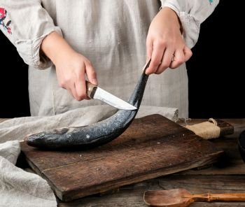 woman in gray linen clothes cleans the fish sea bass scales on a brown wooden board, black background