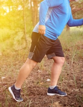 adult plump athlete in blue uniform, sneakers and black shorts runs through the middle of the woods on a summer evening,  concept of outdoor sports and a healthy lifestyle
