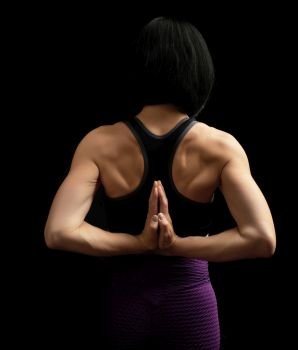 young woman with a sports figure and muscles joined her hands behind her back, hands makes a gesture of namaste, low key