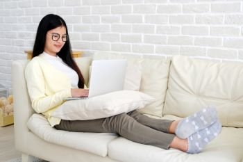Young asian woman using laptop computer sitting  on sofa at home living room background, working at home, people and technology, lifestyles, education, business concept