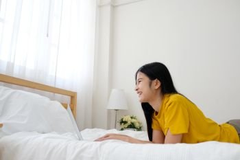 Young asian woman using laptop computer on bed in her bed room background with copy space, working at home, people and technology, lifestyles, education, business concept