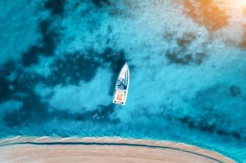 Aerial view of the white yacht in the clear blue water at sunset in summer. Top view from drone of boat, sandy beach. Indian ocean. Travel in Zanzibar, Africa. Tropical landscape with motorboat, sea. Aerial view of the white yacht in the clear blue water at sunset