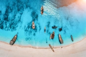 Aerial view of the fishing boats in clear blue water at sunset in summer. Top view from drone of boat, sandy beach. Indian ocean. Travel in Zanzibar, Africa. Tropical landscape with sailboats, sea. Aerial view of the fishing boats in clear blue water at sunset