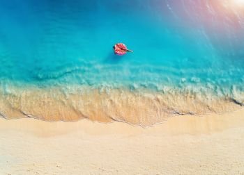 Aerial view of a young woman swimming with the donut swim ring in the clear blue sea with waves at sunrise in summer. Tropical aerial landscape with girl, azure water, sandy beach. Top view. Travel. Aerial view of a young woman swimming with the donut swim ring 