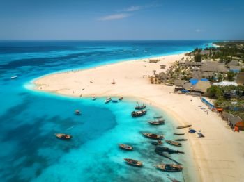 Aerial view of the fishing boats on tropical sea coast with sandy beach at sunny day. Summer holiday on Indian Ocean, Zanzibar, Africa. Landscape with boat, buildings, transparent blue water. Top view