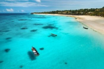 Aerial view of boats on tropical sea coast with sandy beach at sunny day. Summer holiday on Indian Ocean, Zanzibar, Africa. Landscape with boat, palm trees, transparent blue water, sky. Top view