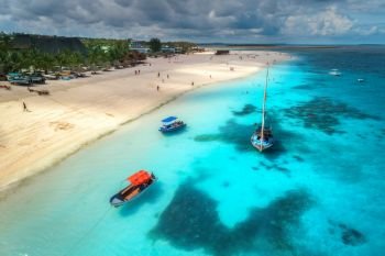Aerial view of boats on tropical sea coast with sandy beach at sunny day. Summer holiday on Indian Ocean, Zanzibar, Africa. Landscape with boat, palm trees, transparent blue water, sky. Top view