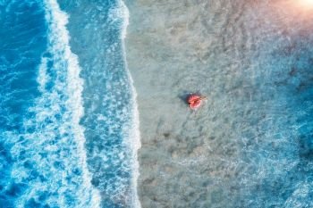 Aerial view of a young woman swimming with the pink donut swim ring in the clear blue sea with beautiful waves at sunset in summer. Tropical aerial landscape with girl, azure water. Top view. Travel
