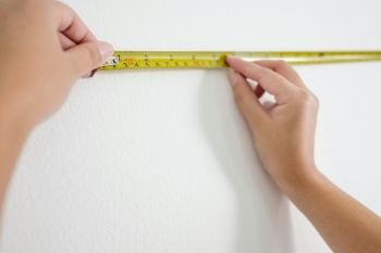 Hands of woman use Measuring yellow Tape on the white wall.