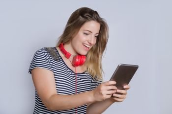 Portrait of young beautiful woman with red earphones and using a digital tablet in studio.