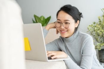 Asian woman is working on a laptop in home . On her face are smile when she work at sofa.