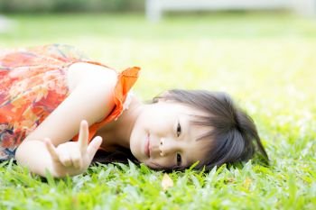 Beautiful portrait little girl asian of a smiling lying on green grass at the park, kid  leisure and joyful in outdoor.