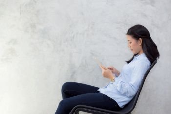 Beautiful young asian woman touching tablet computer and smile sitting on cement background, freelancer female calling telephone, communication concept.