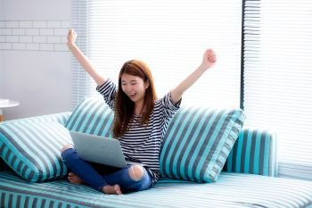 Beautiful happiness portrait of young asian woman using laptop work with success on sofa in the home, girl and notebook internet online with glad, communication concept.