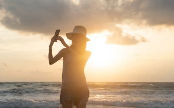Happy Asian woman taking a selfie to post on social media at beach during travel holidays vacation outdoors at ocean or nature sea at sunset time, Phuket, Thailand