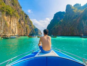 An Asian man, a tourist, sitting on a boat to snorkeling or diving in Krabi with blue turquoise seawater, Phuket island in summer season during travel holidays vacation trip. Andaman ocean, Thai