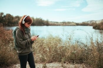 Young woman using her smartphone near a lake with headphones