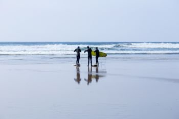 Surfers, with surfboards, on a wet beach in Cornwall, UK