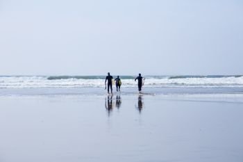 Surfers, carrying surfboards, walking into the water in Cornwall, UK