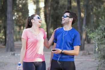 Image of excited man and woman with headphones listening to music on cell phones in the park