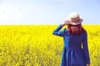 Happy girl in a hat walking in amazing field of yellow rapeseed in the countryside. Emotions
