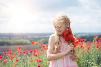  Happy little smiling girl in a hat  at the amazing field of beautiful red poppy field  in the countryside.
