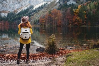 girl with a backpack stands on the shore of a mountain lake
