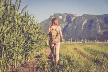 Young girl in jumpsuit with backpack is taking a walk on a field, summer time