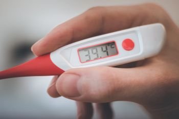 Man holds a red fever thermometer with 39 degrees Celsius in his hand