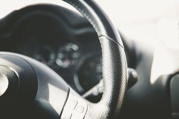 Leather-black steering wheel of a modern car, blurry dashboard