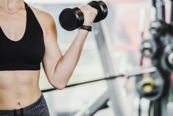Athletic woman doing biceps muscle  workout with dumbbell in close-up at the gym ( copy space).
