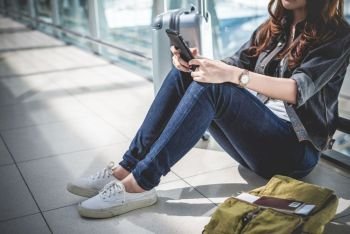 Close up of young woman with bag and suitcase luggage waiting for departure while sitting in airport lounge. Female traveler and tourist theme. High season and vacation concept. Relax and lifestyles