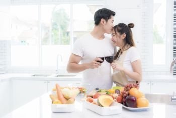 Asian lovers in kitchen, Man give forehead kiss to woman while clink wine glasses to each other. Family and Couple concept. Honeymoon and Holidays theme