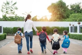Group of preschool student and teacher holding hands and walking to home. Mom bring her children go to school together. Back to school and Education concept. People and lifestyles theme. Back view 