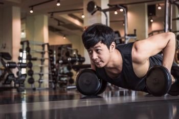 Portrait of Asian fitness man doing pushing up exercise with dumbbell in gym. People lifestyle and Sport concept. Sportsman holding weight by two hands on floor.