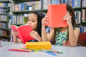 Two little cute girls multi-ethnic friends reading books together in school library. People lifestyles and Education learning concept. Happy friendship kids doing leisure activity for examination test
