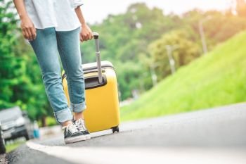 Closeup lower body of woman handling yellow trolly luggage along road trip with mountain hill background. Freedom girl on road way in summer. People lifestyles and transportation travel concept.