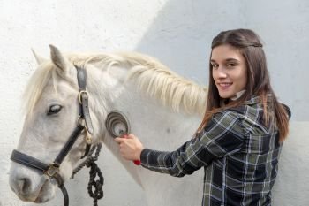 smiling young woman rider brushing the white horse