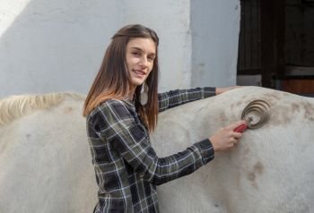 smiling young woman rider brushing the white horse