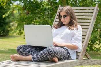 pretty teenage girl sitting in the deck chair using laptop