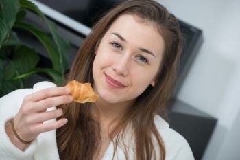 at morning, young and smiling woman eating a pastry