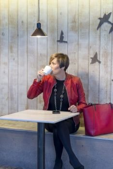 Elegant woman with red jacket sitting in a cafe drinking coffee.