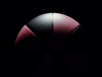 Pink and black colored single basketball for women or men sitting on black background. Light shining directly on basketball from top. dramatic lighting