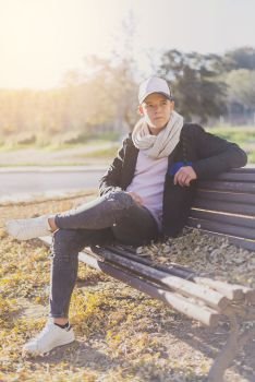 Stylish teenager sitting on a wooden bench on a city street casual wearing
