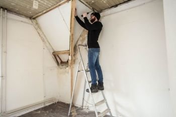 Handyman standing on a ladder and renovating a home, using tools like a hammer concept renovating new home. Handyman standing on a ladder and renovating a home, using tools like a hammer