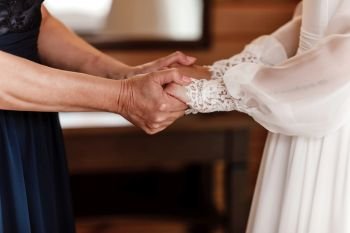 Bride on wedding day holding her mother’s hands. Concept of relationship between moms and daughters. an old woman holds her young daughter married. Bride on wedding day holding her mother’s hands. an old woman holds her young daughter married. Concept of relationship between moms and daughters