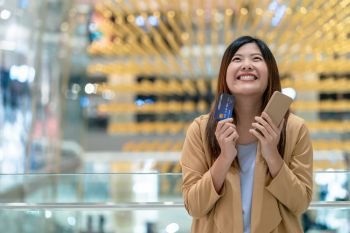 Portrait Asian woman happiness when holding credit card and mobile phone for online shopping in department store over the clothes shop background, technology money wallet and online payment concept
